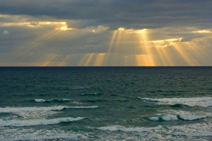 Sunbeams - beams of light break through a dense bank of black clouds over the ocean Sunbeams - beams of light break through a dense bank of black clouds over the ocean