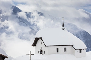 Clouds above the mountain huts and church covered with snow, Bettmeralp, district of Raron Clouds above the mountain huts and church covered with snow, Bettmeralp, district of Raron