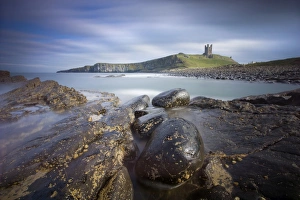 Dunstanburgh Castle bathed in afternoon sunlight with rocky coastline in foreground Dunstanburgh Castle bathed in afternoon sunlight with rocky coastline in foreground