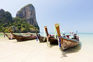 Traditional Longtail boats moored by Railay Beach with limestone cliffs in the background Traditional Longtail boats moored by Railay Beach with limestone cliffs in the background
