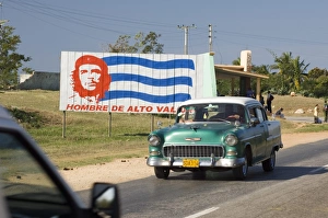 A vintage 1950s American Chevrolet on the road near Trinidad passing a colourful revolutionary road sign, Cuba, West Indies A vintage 1950s American Chevrolet on the road near Trinidad passing a colourful revolutionary road sign, Cuba, West Indies