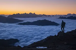 Hiker admiring sunrise from Latemar with Pale di San Martino group in background over a Hiker admiring sunrise from Latemar with Pale di San Martino group in background over a