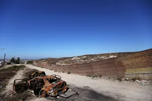 A burnt car is seen next to a section of the wall separating Mexico and the United States A burnt car is seen next to a section of the wall separating Mexico and the United States