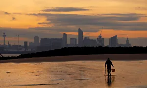 A fisherman digs for bait in front of the Liverpool skyline on the beach at New Brighton A fisherman digs for bait in front of the Liverpool skyline on the beach at New Brighton