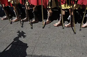Shadow of a penitent carrying a wooden cross on a baton falls on ground as men dressed Shadow of a penitent carrying a wooden cross on a baton falls on ground as men dressed