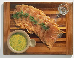 Bowl of sauce and thin slices of pink salmon seasoned with herb sprigs on wooden board Bowl of sauce and thin slices of pink salmon seasoned with herb sprigs on wooden board