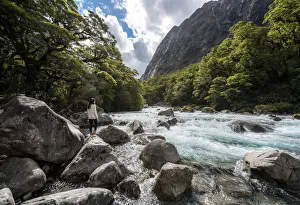 The women stands on a stone in the midst of watercourse with mountains in Milford highway The women stands on a stone in the midst of watercourse with mountains in Milford highway