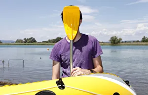 Young man holding paddle of rubber dinghy in front of his face, having fun boating Young man holding paddle of rubber dinghy in front of his face, having fun boating